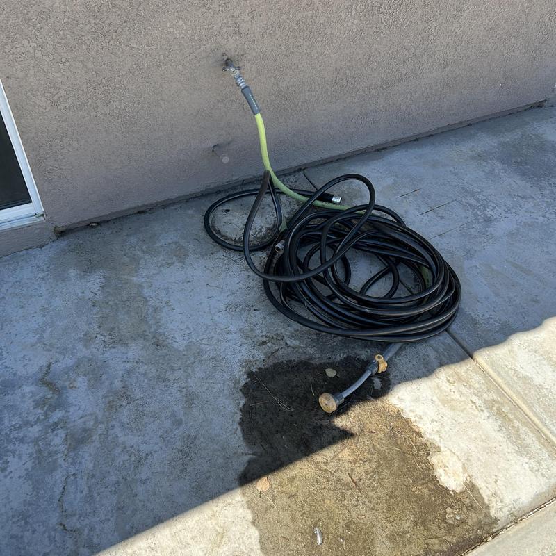 Hose bib with black garden hose on concrete patio