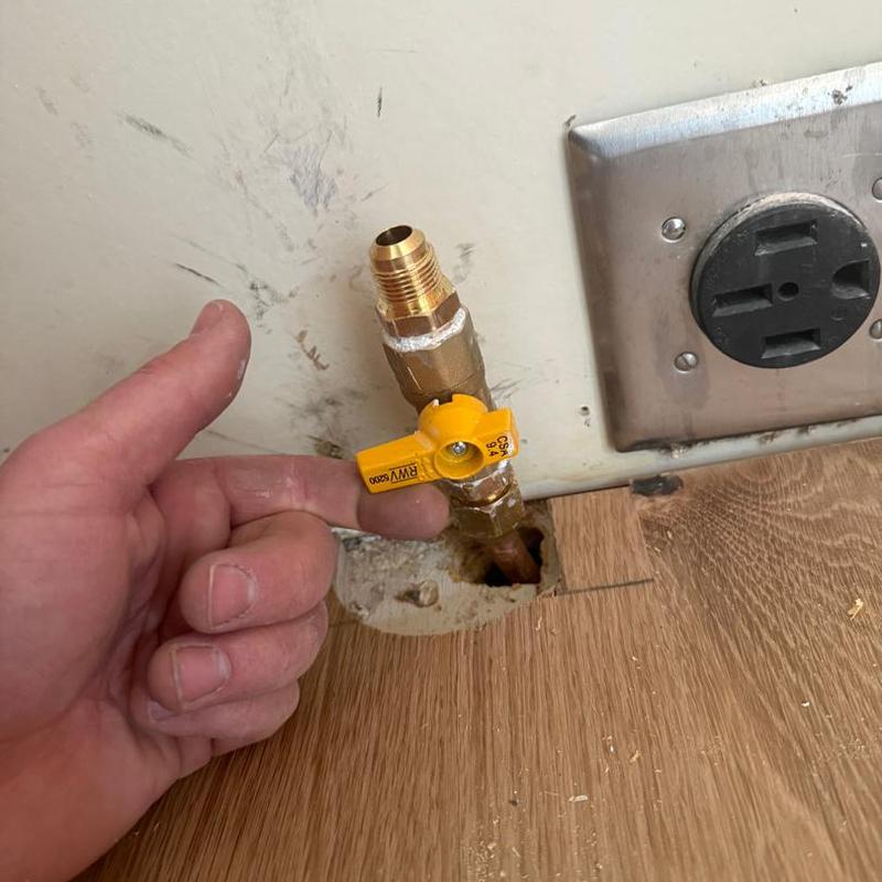 Gas line valve with yellow handle near wall outlet