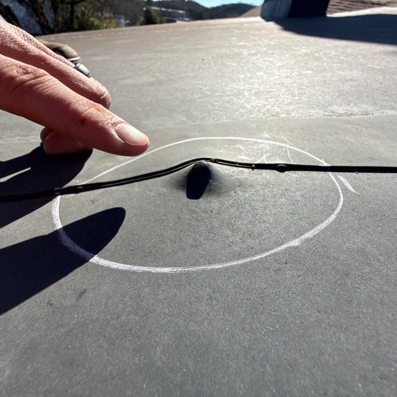 Flat roof membrane blister circled under metal strap