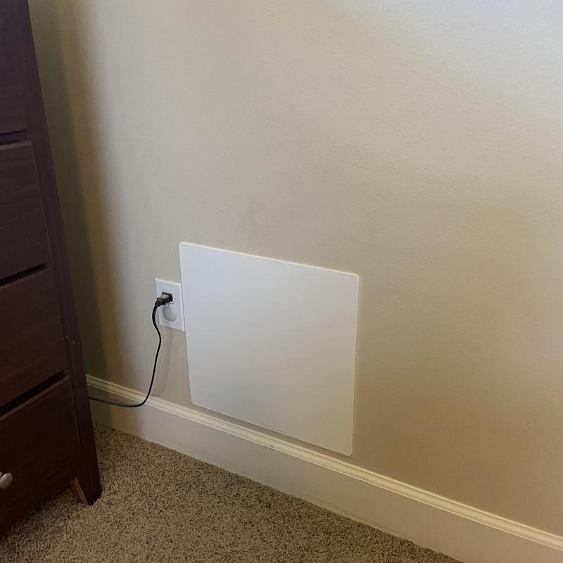 Electric wall heater panel plugged into outlet in bedroom
