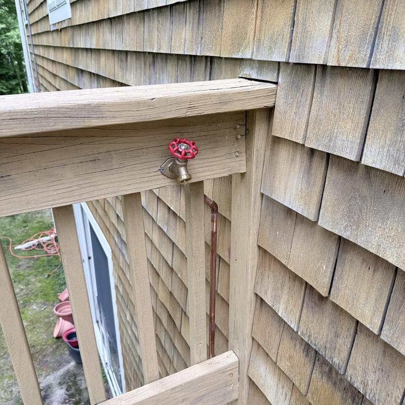 Outdoor silcock on wooden deck railing near house siding