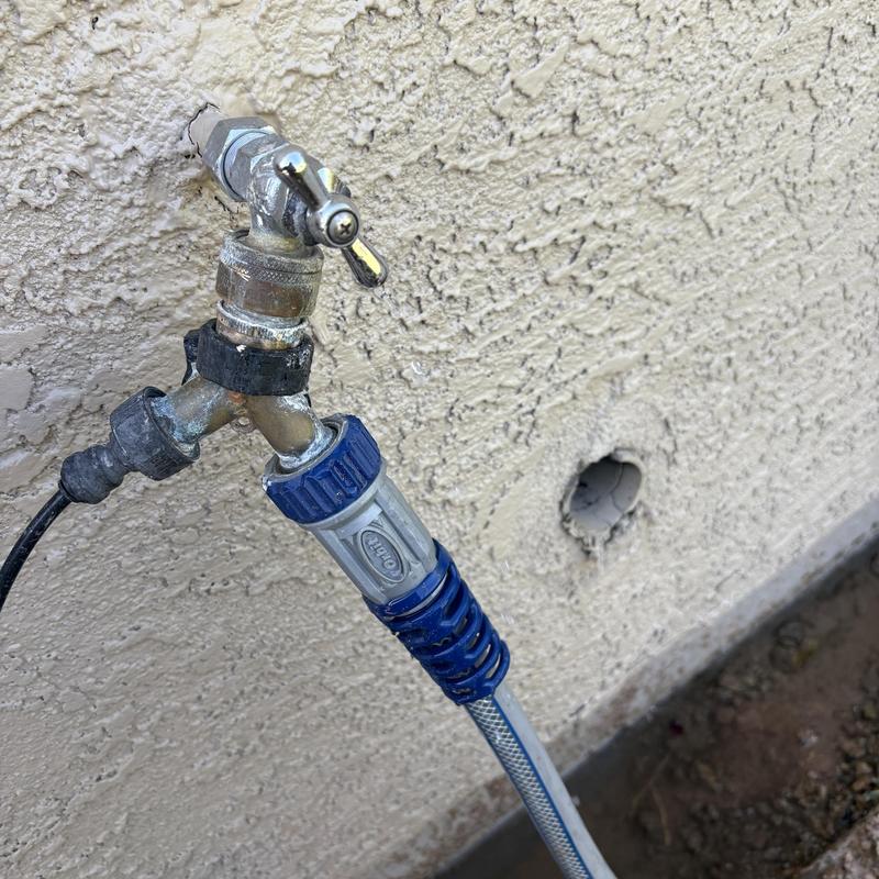 Outdoor faucet with attached garden hose and leak hole