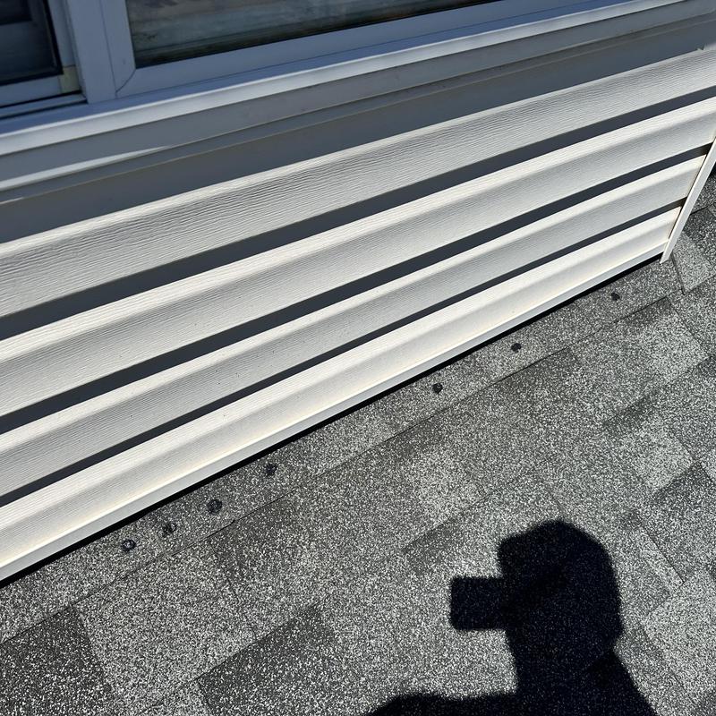 Roof shingles with caulked exposed nail heads near siding