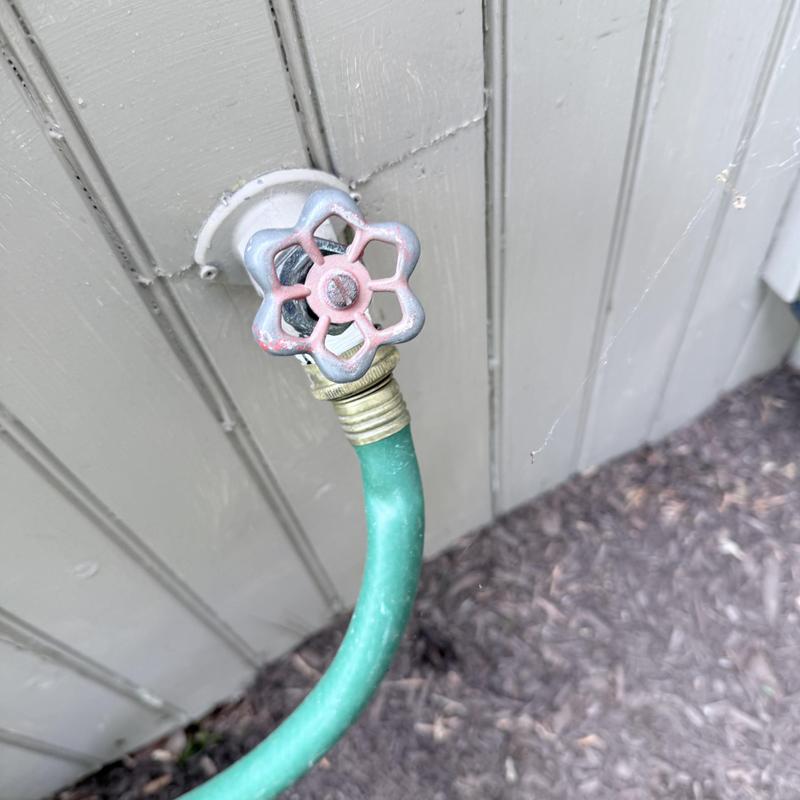 Silcock valve with attached green garden hose outdoors