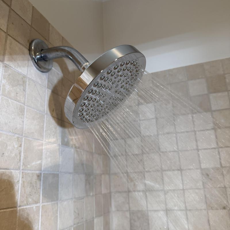 Shower head with flowing water in tiled bathroom