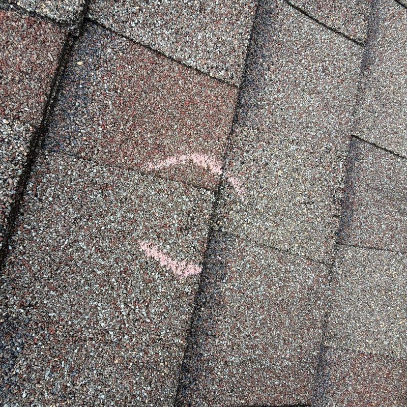 Asphalt shingles with hail damage marked in pink