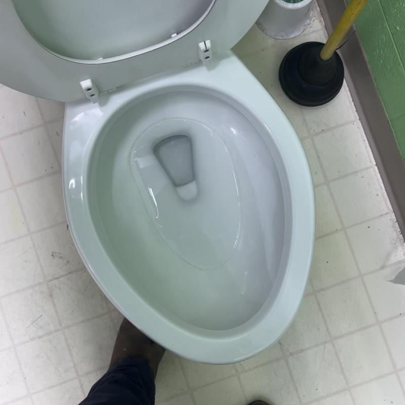 Toilet bowl with plunger on tile floor in bathroom