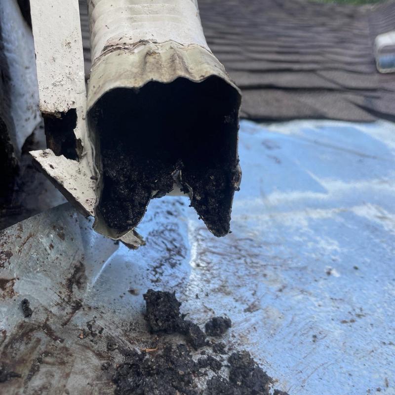 Damaged metal gutter downspout with debris buildup