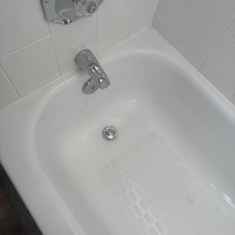 Tub drain and faucet assembly in white tiled bathroom