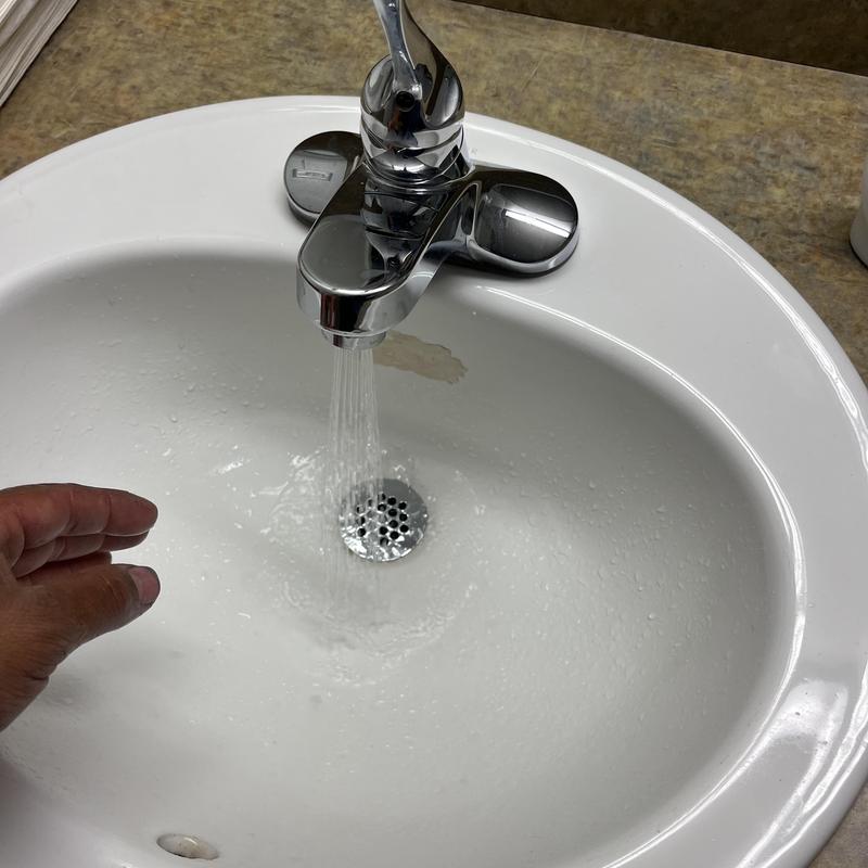 Bathroom sink faucet flow inspection with hand nearby