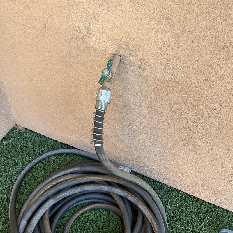 Outdoor hose bib with attached garden hose on wall