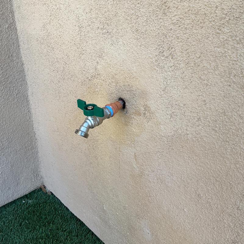 Outdoor hose bib with green handle on stucco wall