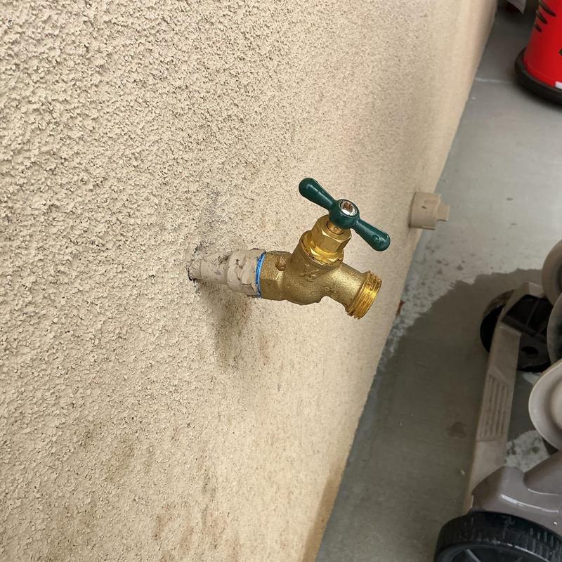 Backyard hose bib with green handle on stucco wall