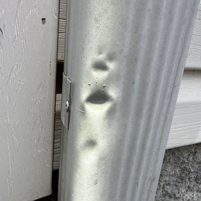 Metal downspout with hail damage dents visible