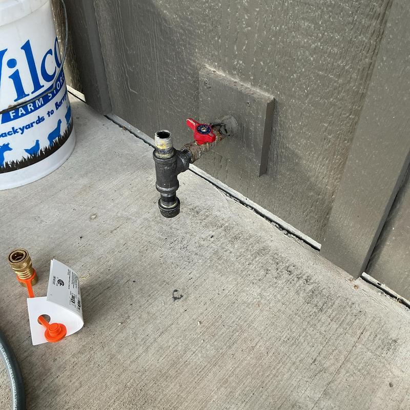 Gas line drip leg with red valve on wall outdoors