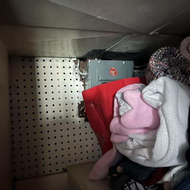 Electrical disconnect box behind laundry items in closet