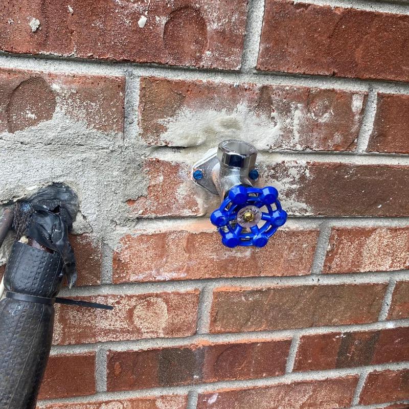 Hose bib with blue valve handle on brick wall