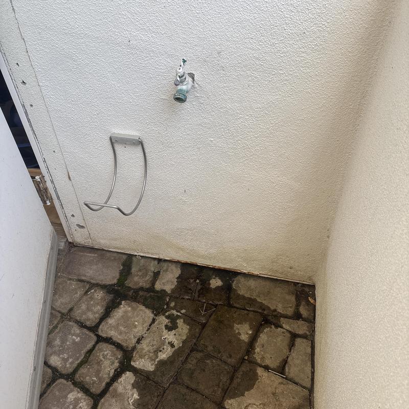 Outdoor hose bib on stucco wall above wet stone patio