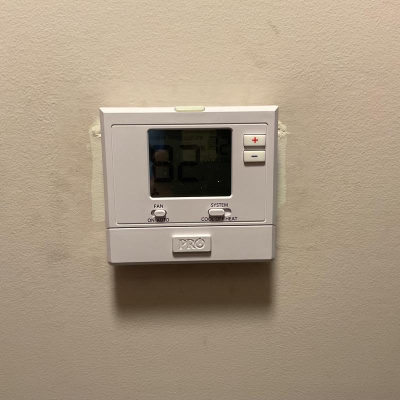 Thermostat control panel on beige wall, 82°F displayed Thermostat control panel on beige wall, 82°F displayed