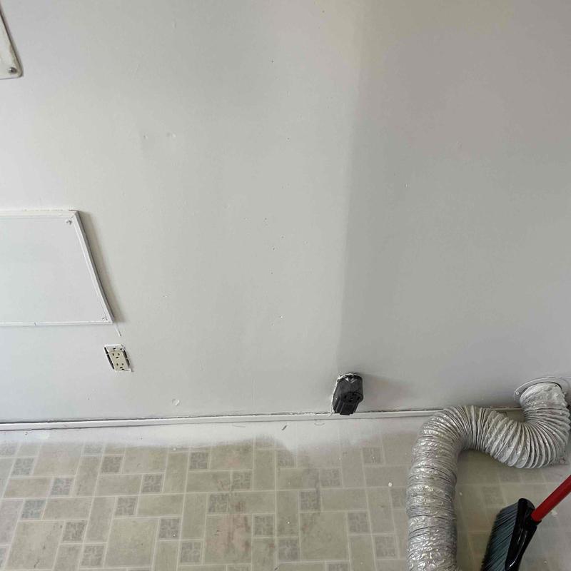 Gas dryer vent hose and wall outlet with broom nearby