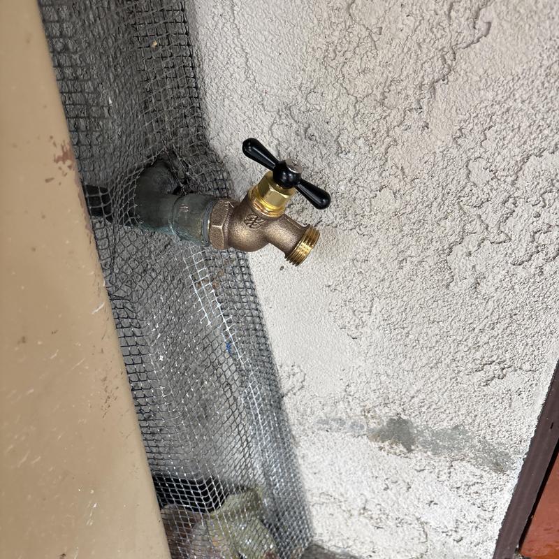 Hose bib with black cross handle on exterior wall Hose bib with black cross handle on exterior wall