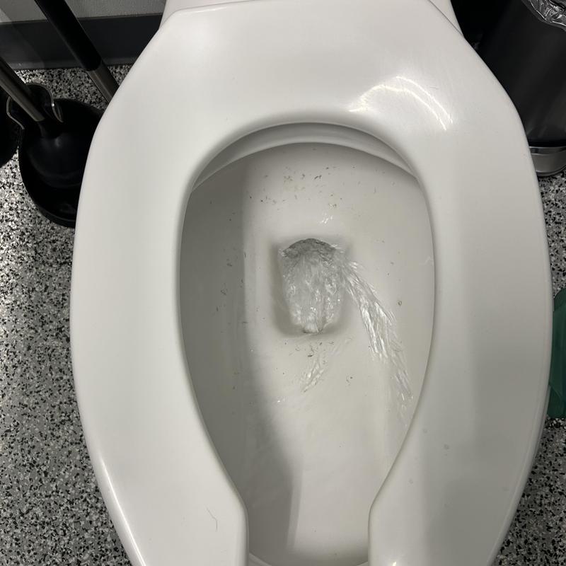 Commercial toilet flushing water flow with plunger nearby