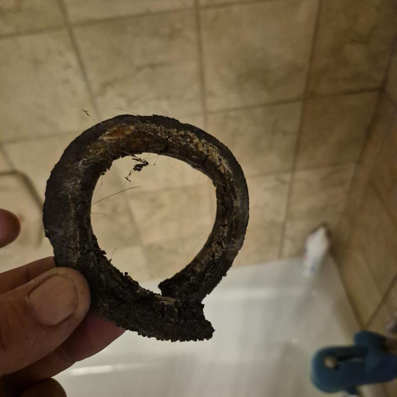 Rusty pipe gasket held in hand against tiled wall background
