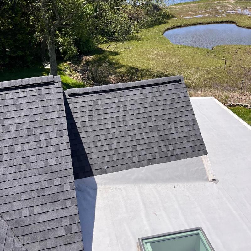 Asphalt shingle roof section next to flat roof with skylight Asphalt shingle roof section next to flat roof with skylight