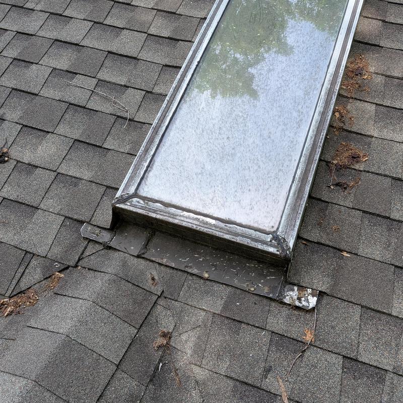 Skylight metal flashing with worn shingles on roof