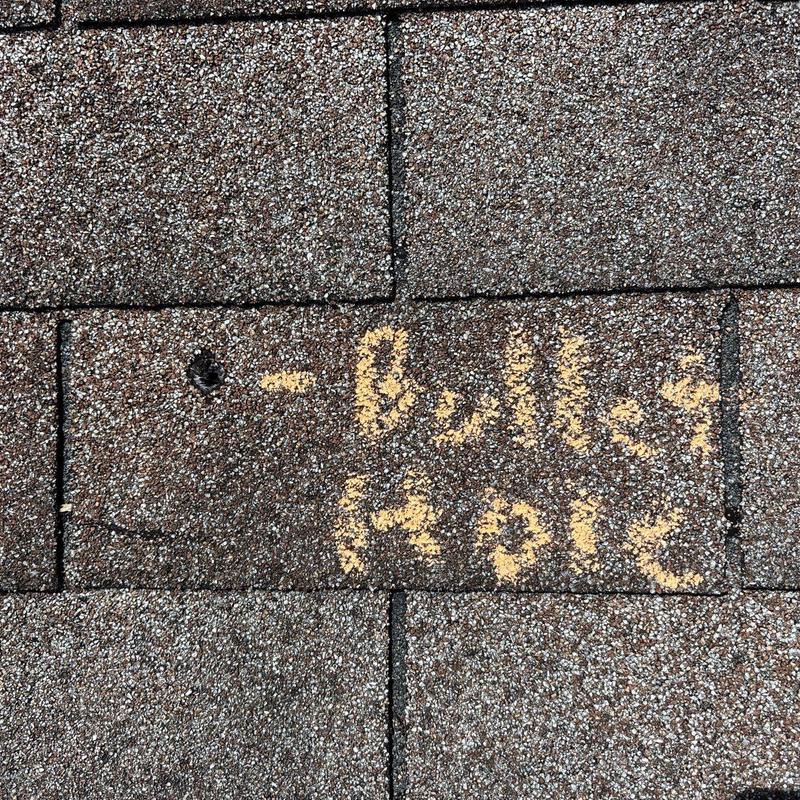 Roof shingle with projectile impact hole marked for repair