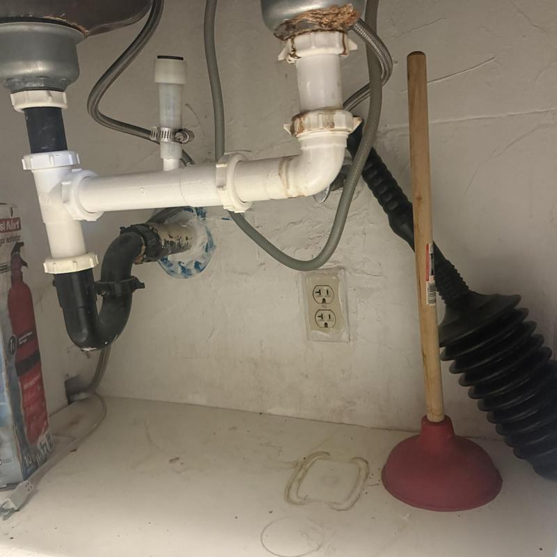 Kitchen sink drain pipes under sink with plunger nearby
