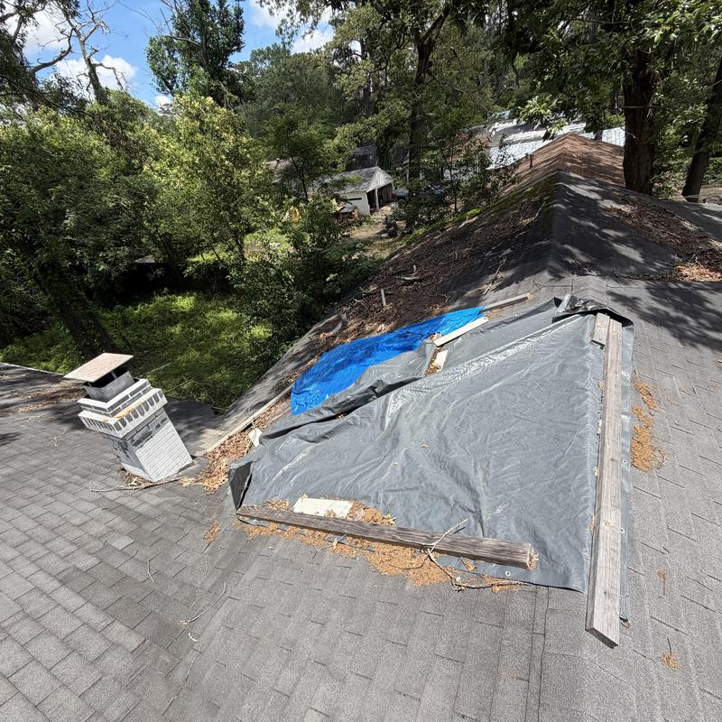 Roof tarp over damaged shingles with chimney nearby