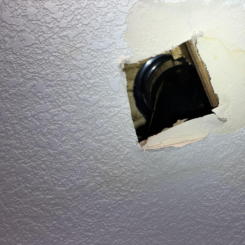 Ceiling drywall with hole exposing pipe and wood framing