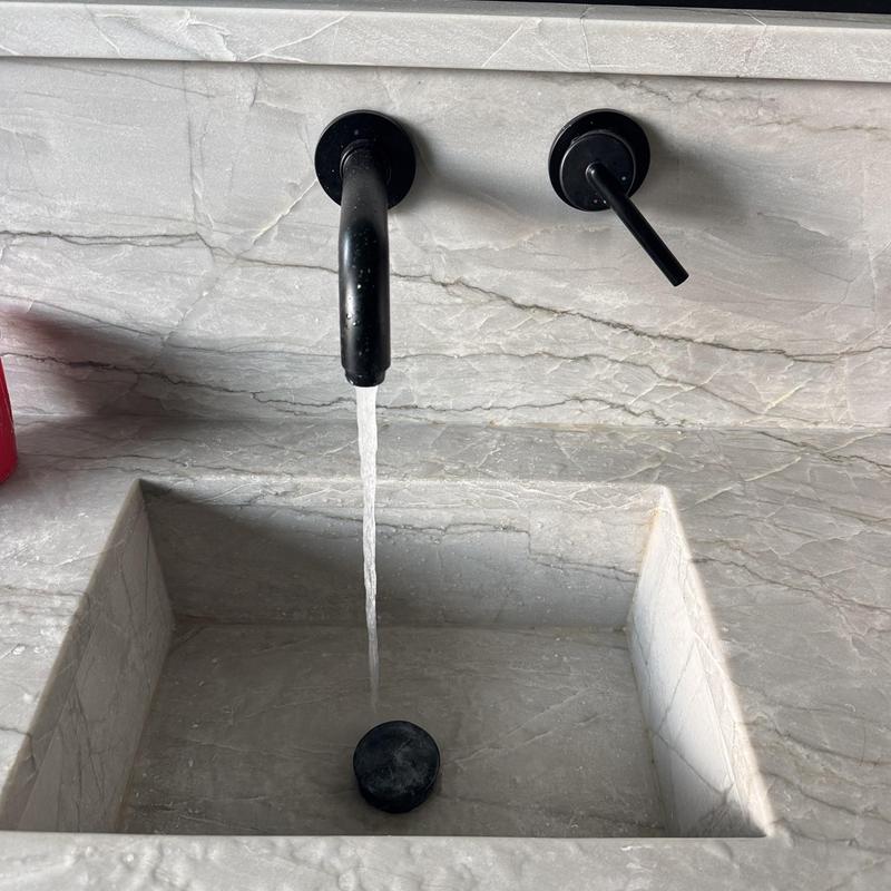 Wall-mounted black faucet running over stone sink basin