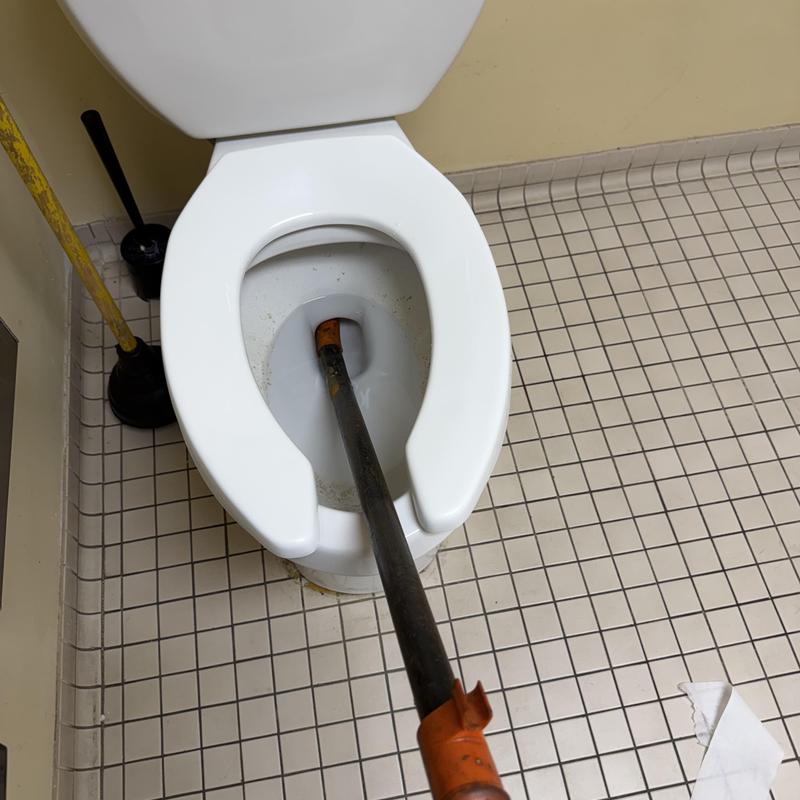 Toilet auger inserted for clog removal in restroom Toilet auger inserted for clog removal in restroom