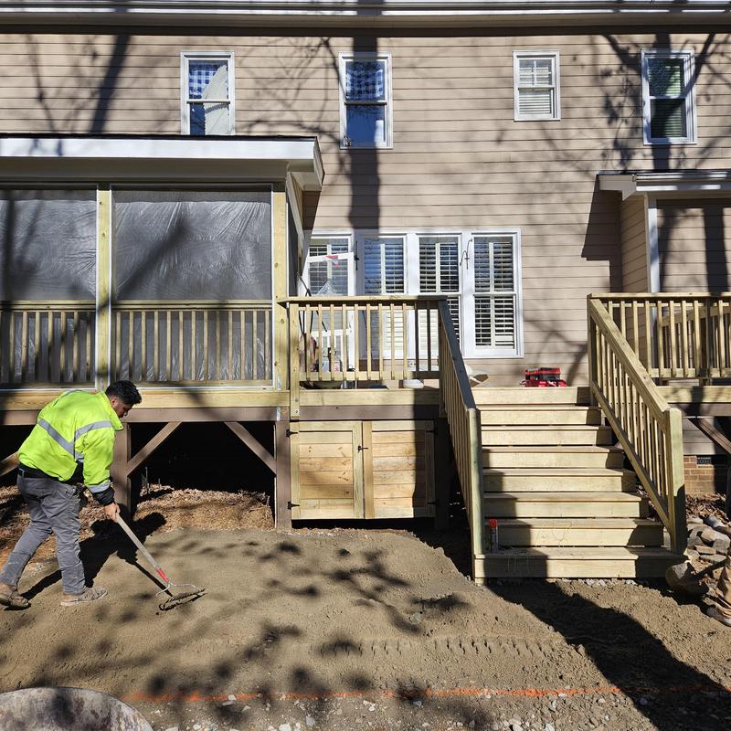 Wood deck with stairs under construction and worker leveling ground Wood deck with stairs under construction and worker leveling ground