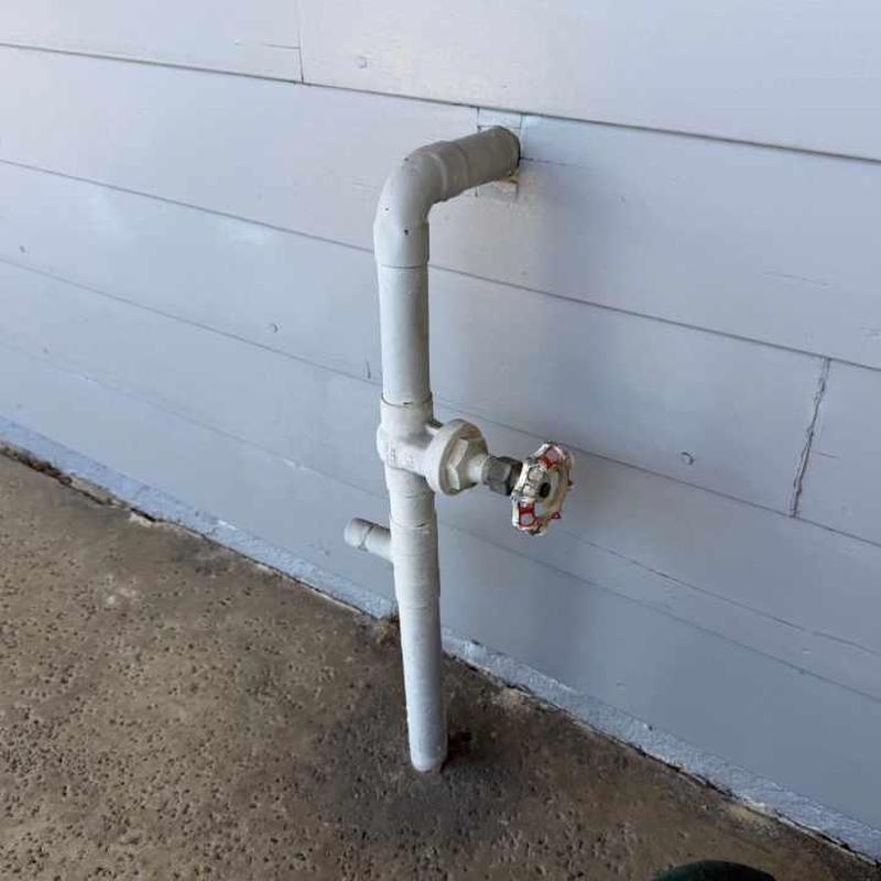 Copper water main valve with red gate handle outdoors