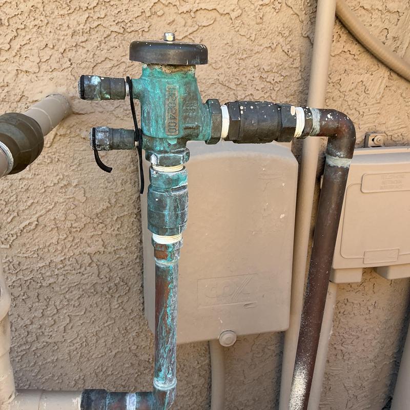 Pressure vacuum breaker with copper pipes against stucco wall