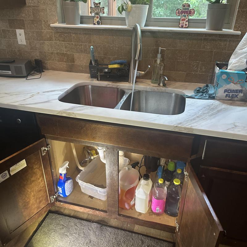 Kitchen sink drain line with open cabinet and flowing water