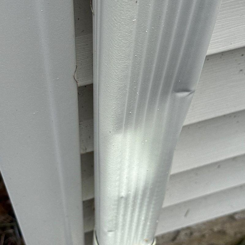 Downspout with hail damage dents on siding exterior