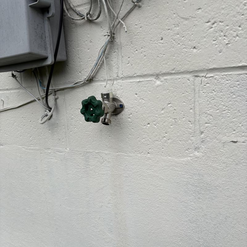 Outside faucet with green handle installed on wall