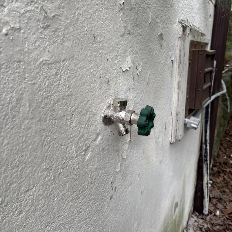 Outside faucet with green handle installed on wall