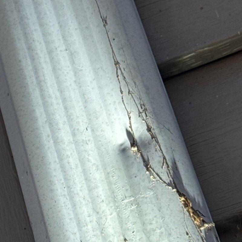 Metal gutter with visible crack and damage from hail impact
