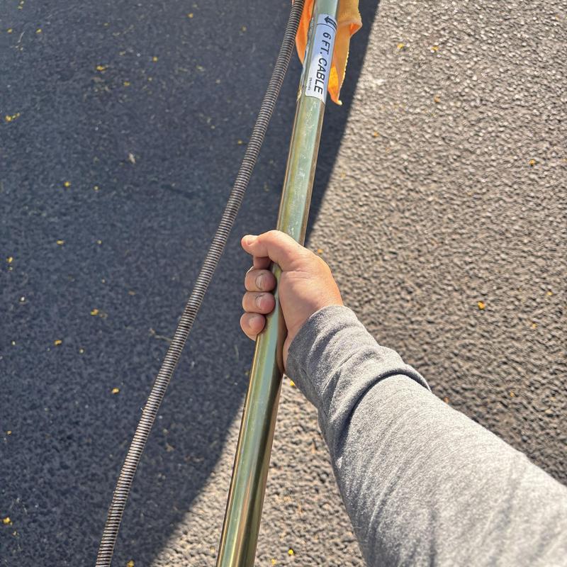 Toilet auger cable held by plumber on asphalt surface