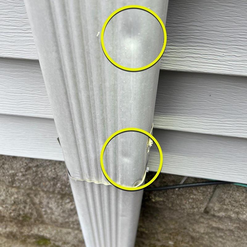 Metal downspout with hail dent damage on siding side