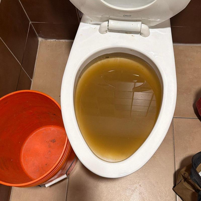 Toilet bowl with clogged dirty water and orange bucket Toilet bowl with clogged dirty water and orange bucket