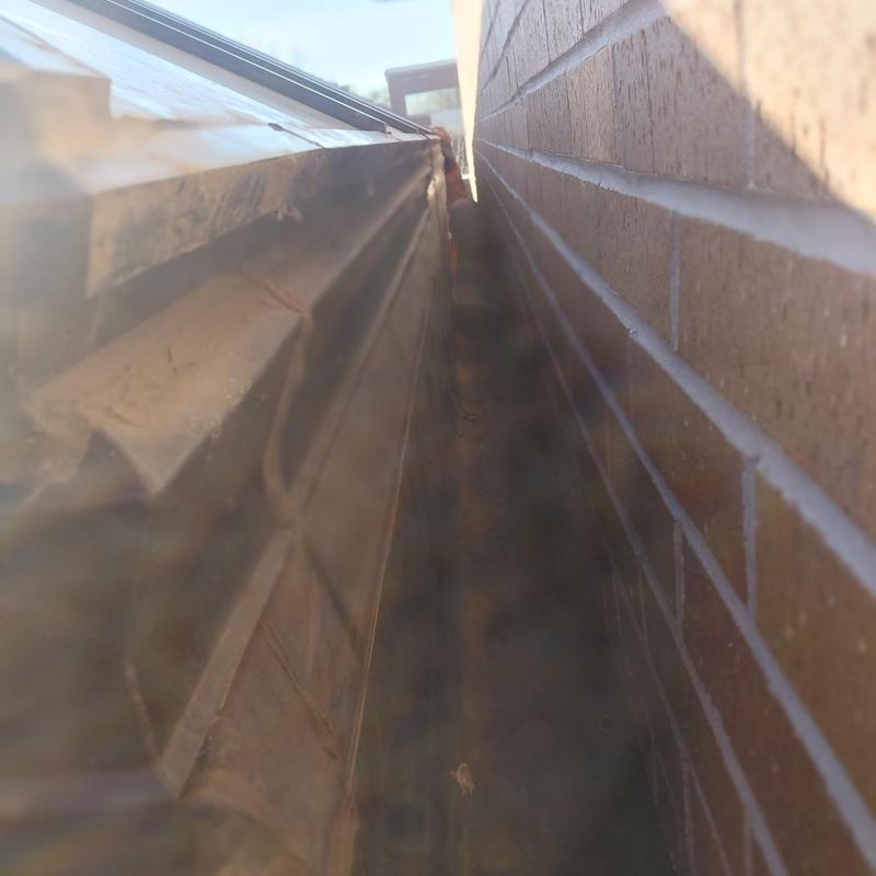 Metal roof gutter and brick wall gap with grime buildup