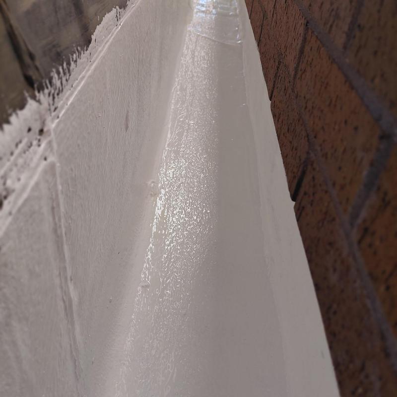 Silicone roof coating on narrow roof edge near brick wall