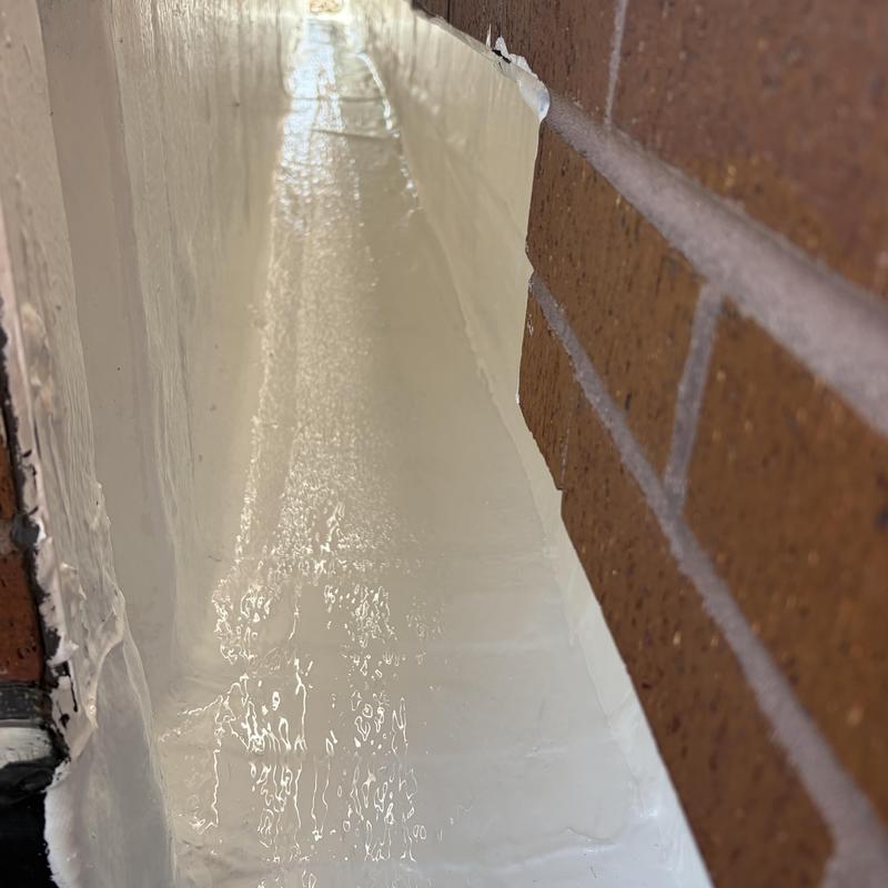Silicone roof coating applied to flashing near brick wall