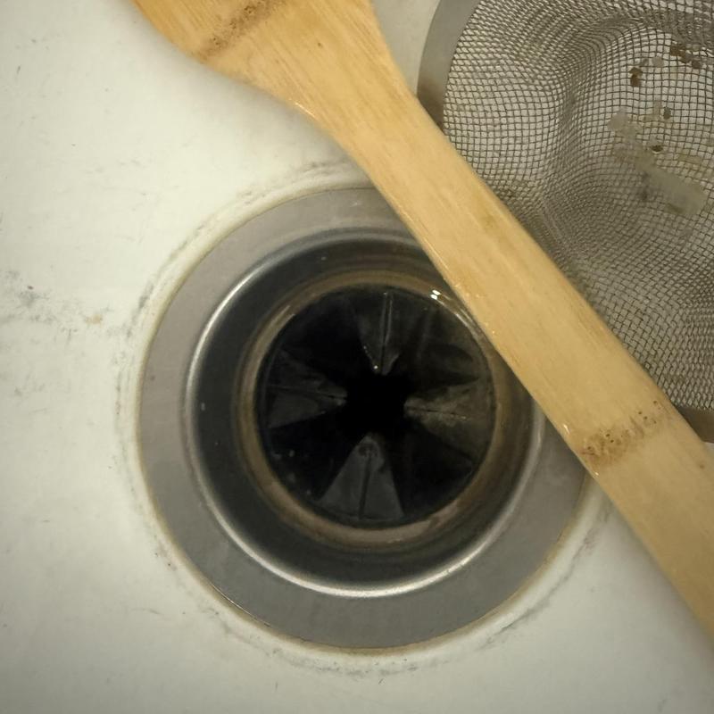 Kitchen sink garbage disposal jammed with wooden spoon nearby